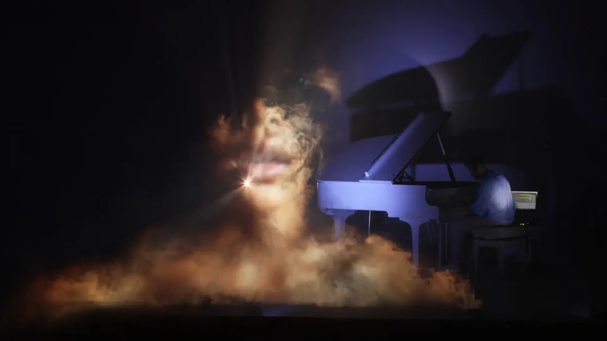 Projected face within warm smoke beside the piano during "Riflesso," a sequence within Per Aria